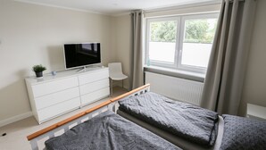 A bedroom with two beds, a TV on a dresser, a chair, and a window with curtains. - Beautiful vacation apartment in Kassel (Kassel)
