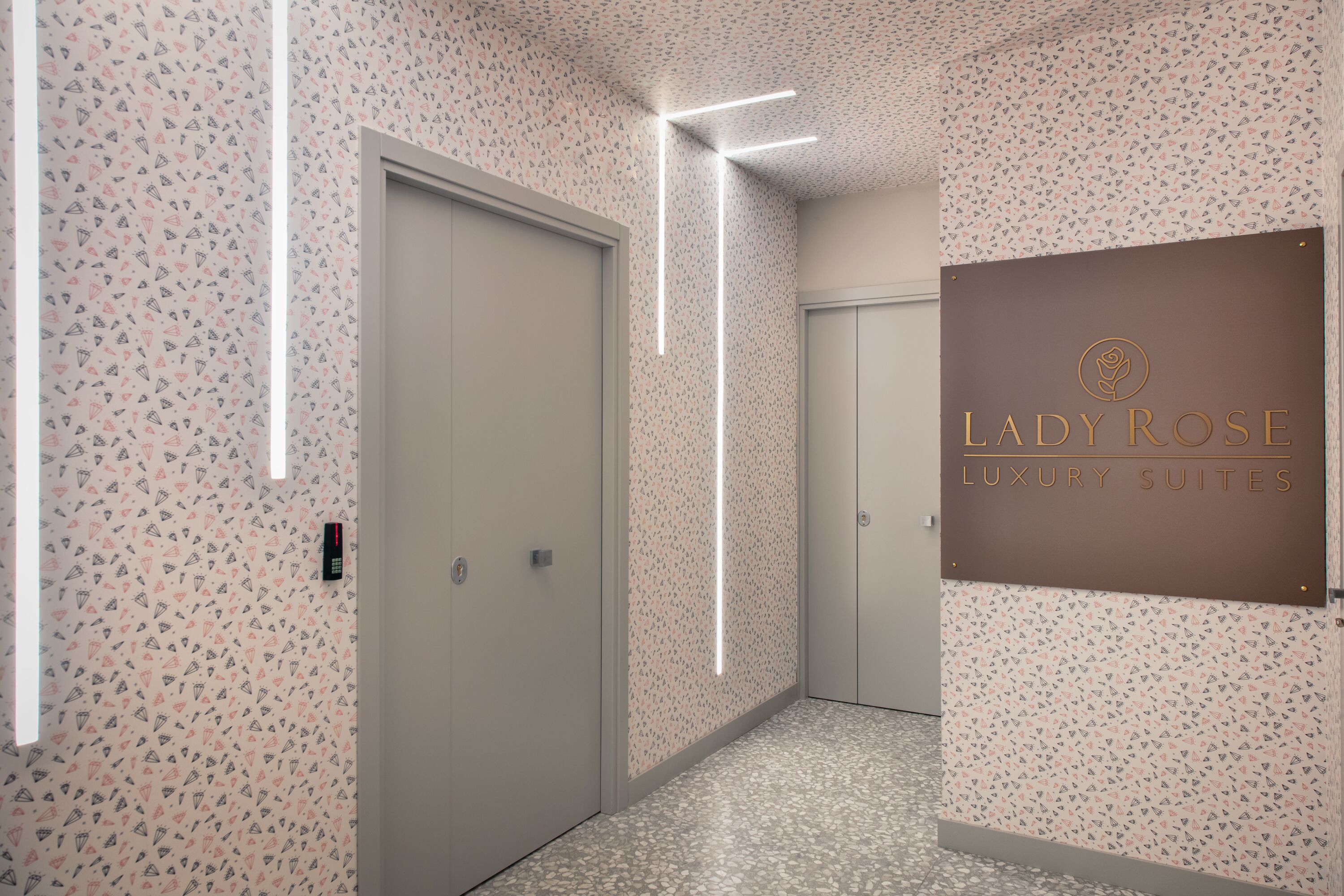Ein Flur mit Wandtapete mit Muster, ein Schild für 'Lady Rose Luxury Suites' und eine moderne Leuchte.