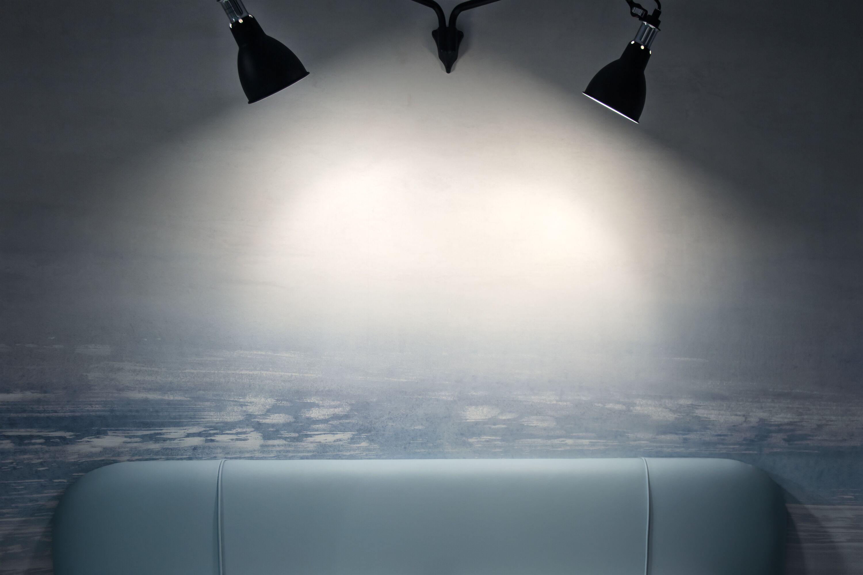 A room with a light-colored sofa, two black lamps, and a textured wall.