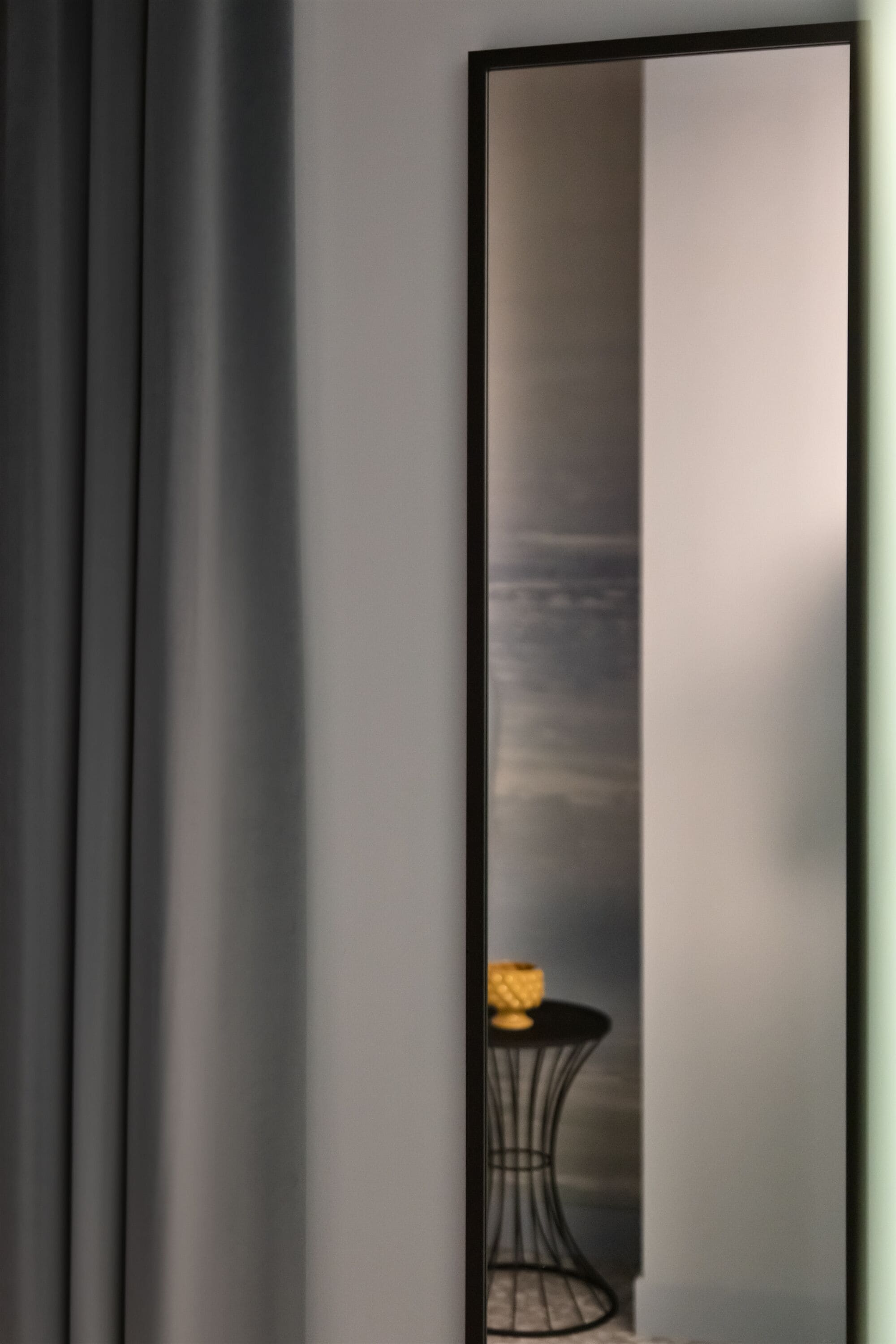 Une pièce dotée d’un grand miroir qui reflète une table sur laquelle se trouve un vase jaune et une chaise noire.