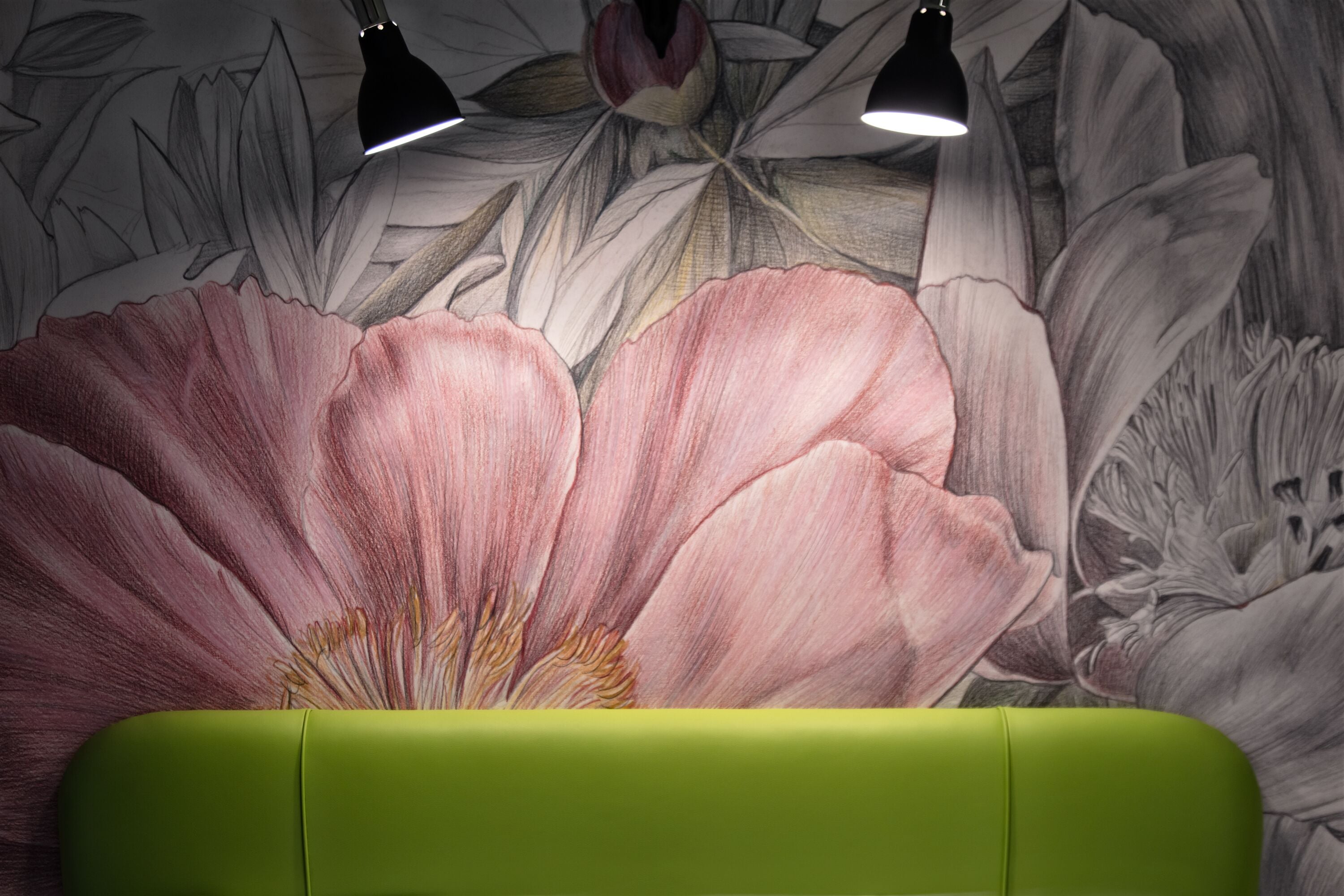 Et værelse med en grøn sofa og et stort blomstermotiv på væggen.