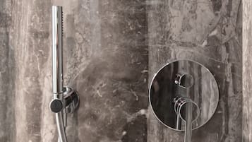 Eine moderne Dusche mit Marmorwand und einer runden Bedieneinheit aus Chrom.