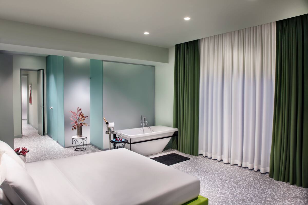 Ett modernt hotellrum med en stor säng, ett badkar och ett separat badrum.