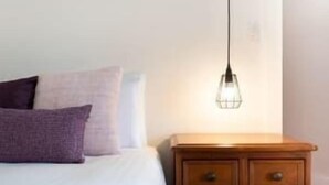 Quarto com cama, mesa de cabeceira de madeira e luminária pendente.