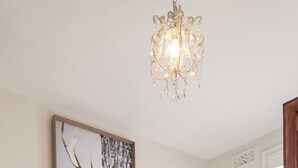 Quarto com cama, um candelabro, quadro de árvore e janela com persianas.