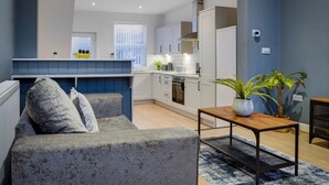 Een moderne woonkamer met een grijze bank, een houten bijzettafeltje en een blauw vloerkleed.
