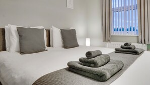 Een hotelkamer met twee bedden, grijze handdoeken en uitzicht op zee door dunne gordijnen.