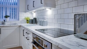 Een moderne keuken met witte kasten, een marmeren aanrechtblad en een inbouwoven.