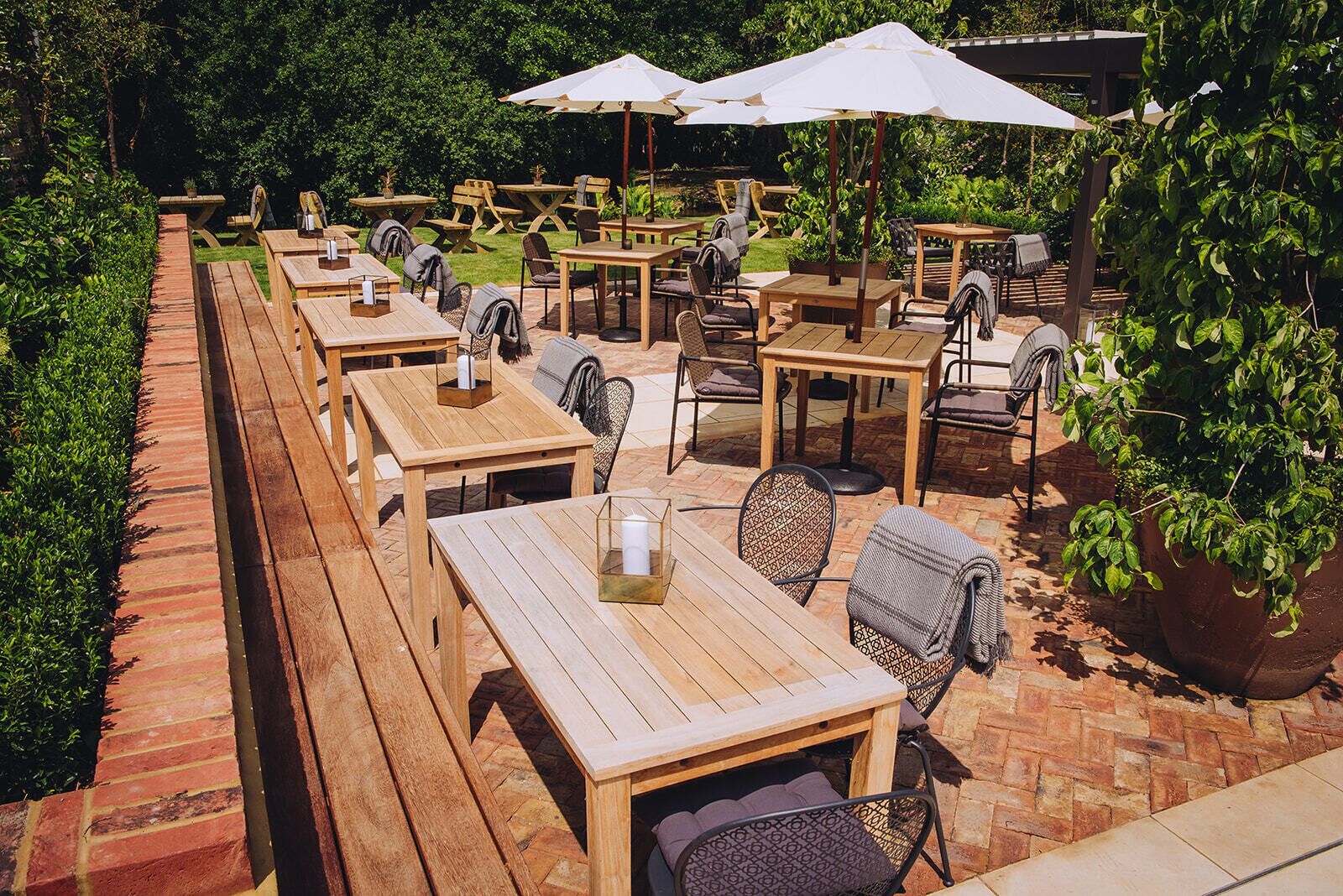 An outdoor patio area with wooden tables and chairs, some with umbrellas.