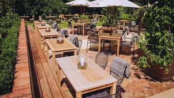 An outdoor patio area with wooden tables and chairs, some with umbrellas.