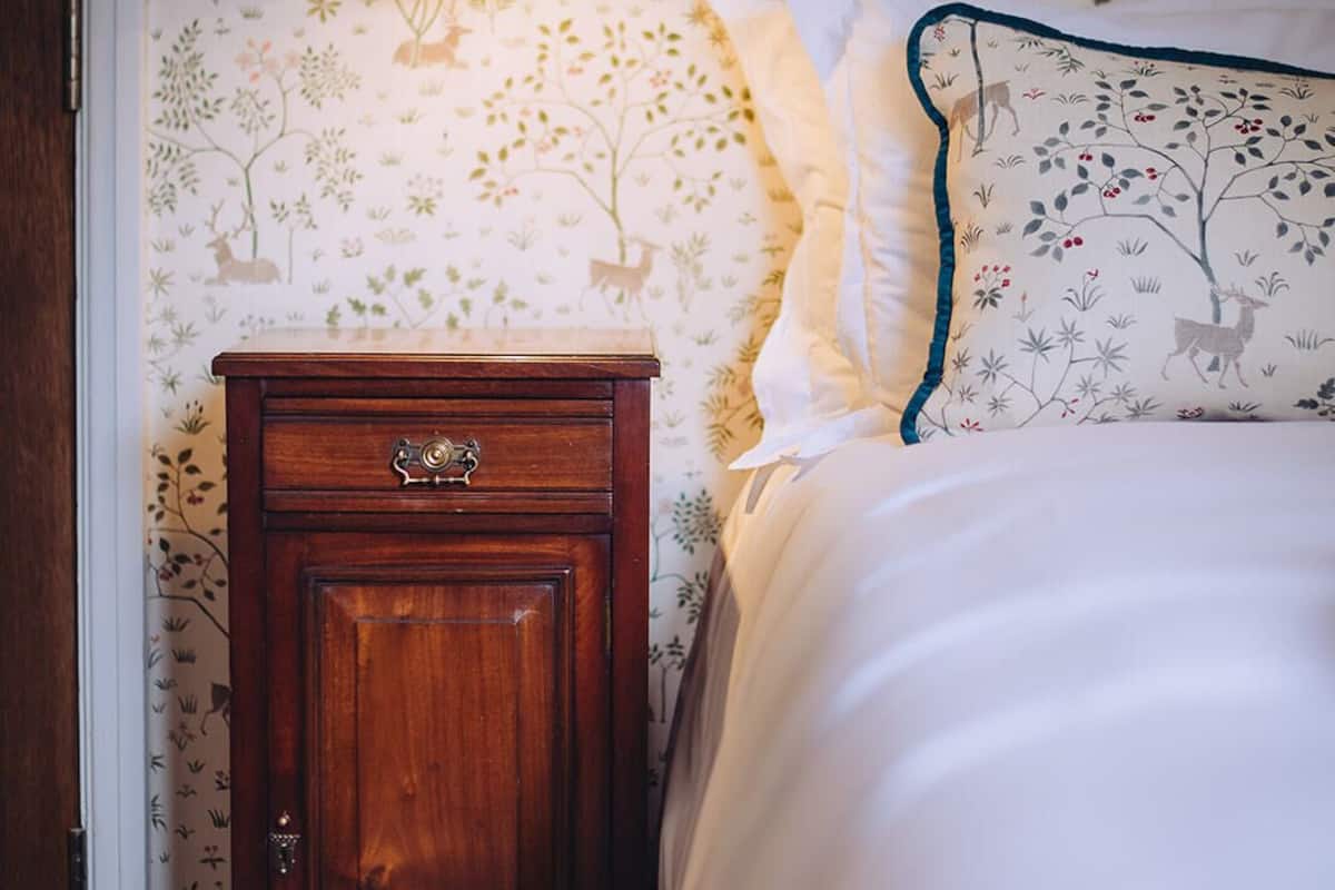 A bedroom with a wooden nightstand, a lamp, and a bed with a patterned wall.