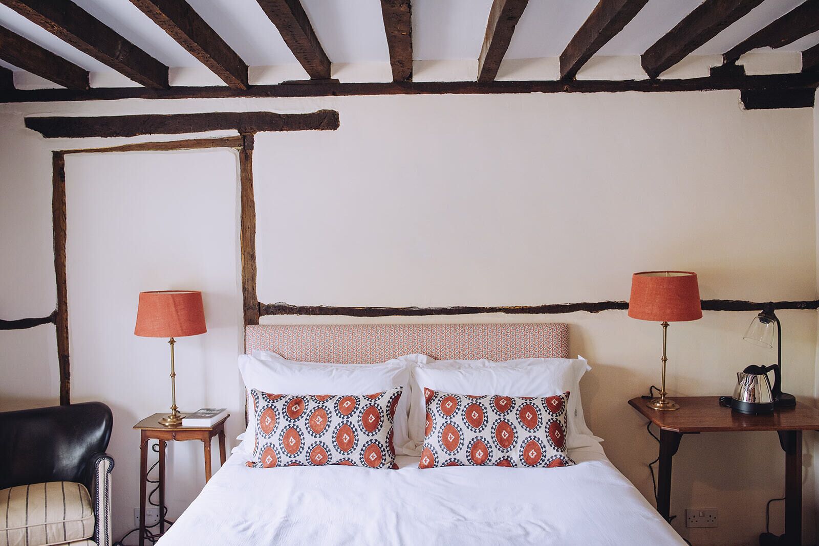 A bedroom with a bed, two bedside tables, a chair, and a wooden ceiling.