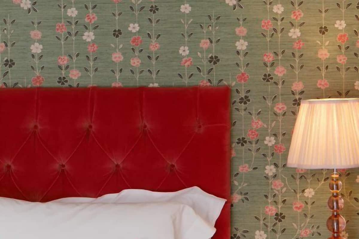 A bed with a red headboard, white and red pillows, and a wooden nightstand with a lamp.