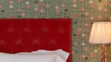 Una cama con cabecera roja, almohadas blancas y rojas, y una mesita de noche de madera con una lámpara.