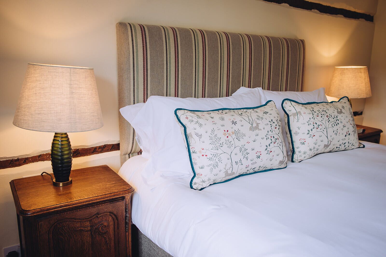 A neatly made bed with white linens and two decorative pillows with floral patterns. There are two bedside lamps on wooden nightstands.