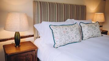 A neatly made bed with white linens and two decorative pillows with floral patterns. There are two bedside lamps on wooden nightstands.