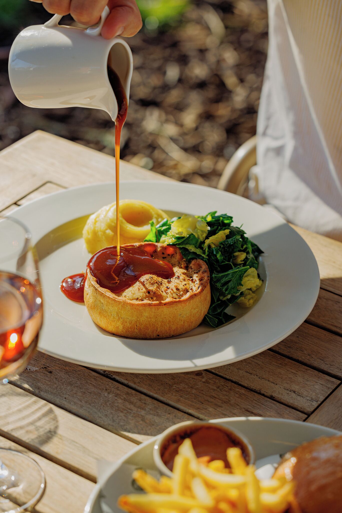 A meal with a baked item topped with sauce, a side of greens, and fries on a white plate.