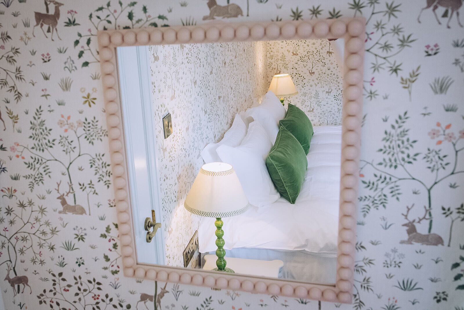Une chambre à coucher avec un lit, des oreillers, une table de chevet, une lampe et un miroir au mur.