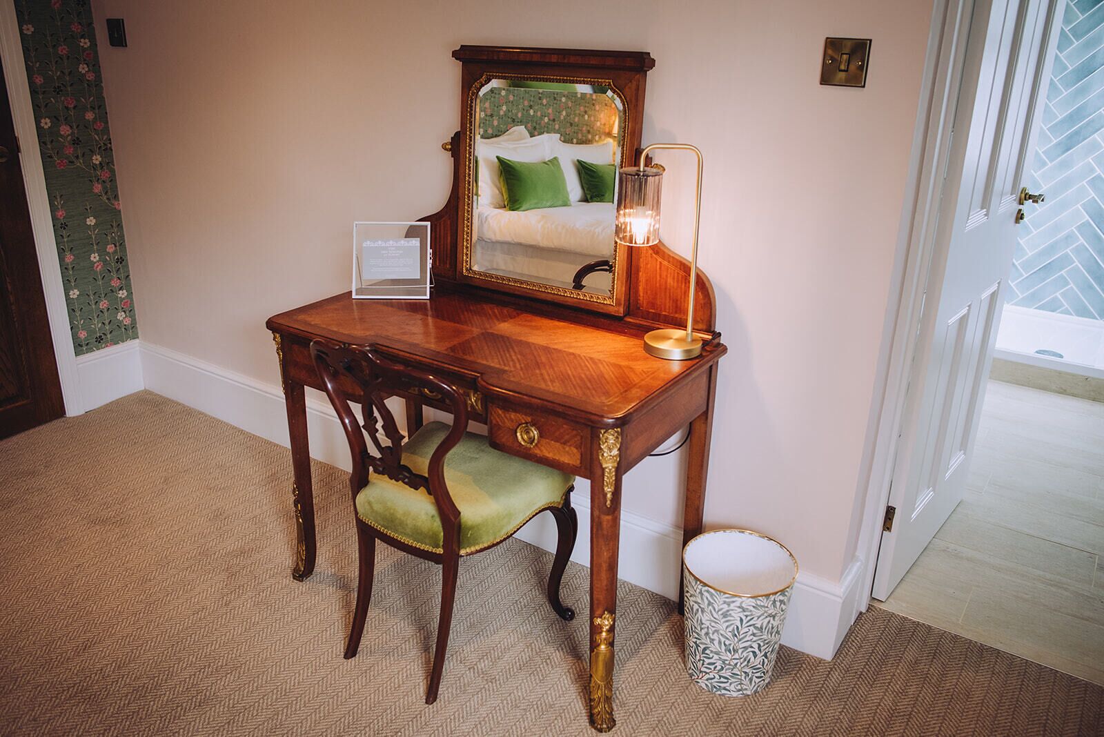 A wooden desk with a mirror, a green chair, and a floor lamp.