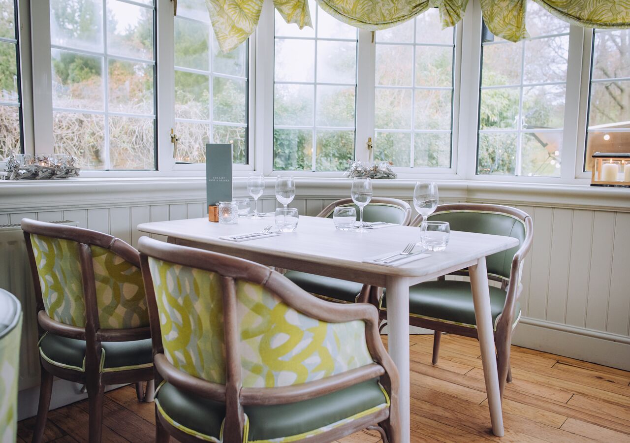 A dining area with a table set for four, surrounded by green upholstered chairs with a patterned design.