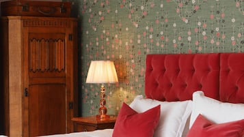 Cama bem arrumada com almofadas vermelhas e brancas, um guarda-roupa de madeira e um papel de parede floral.