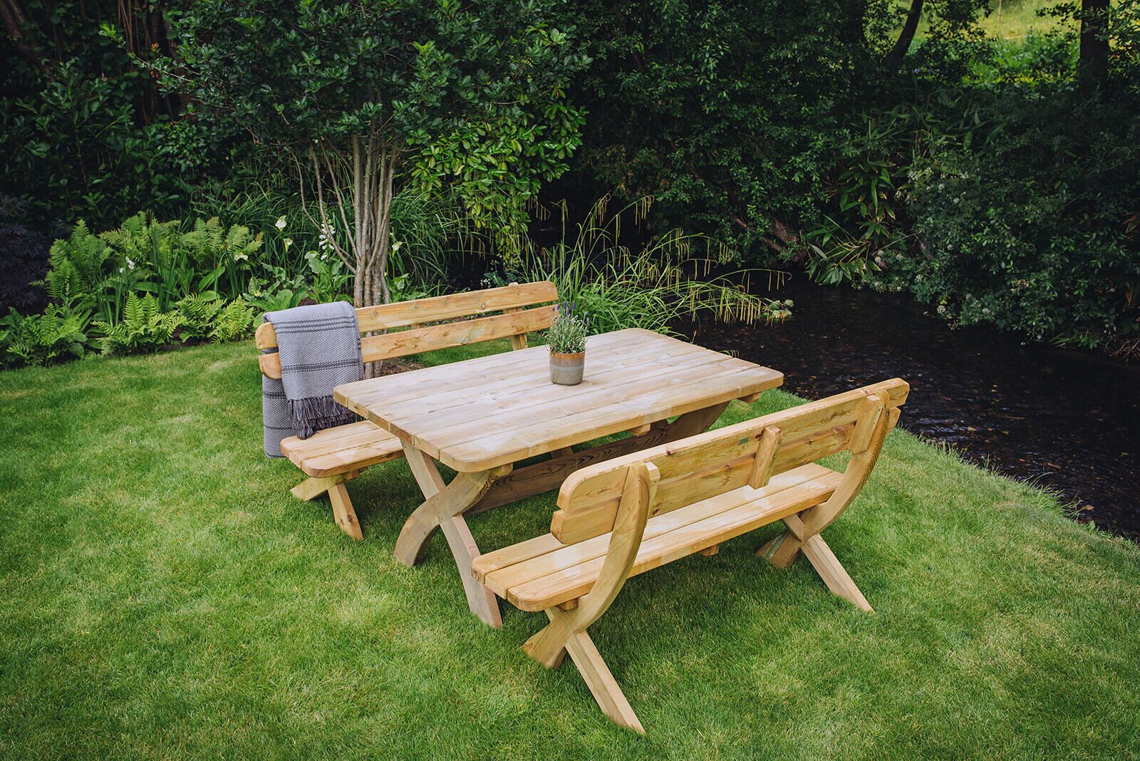 Une table de pique-nique en bois avec des bancs, installée dans un espace jardin verdoyant.