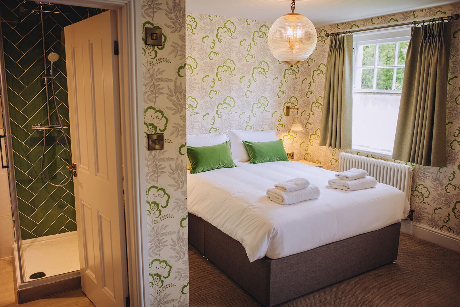 Une chambre d’hôtel avec un grand lit, des oreillers verts, un radiateur et une fenêtre avec des rideaux.