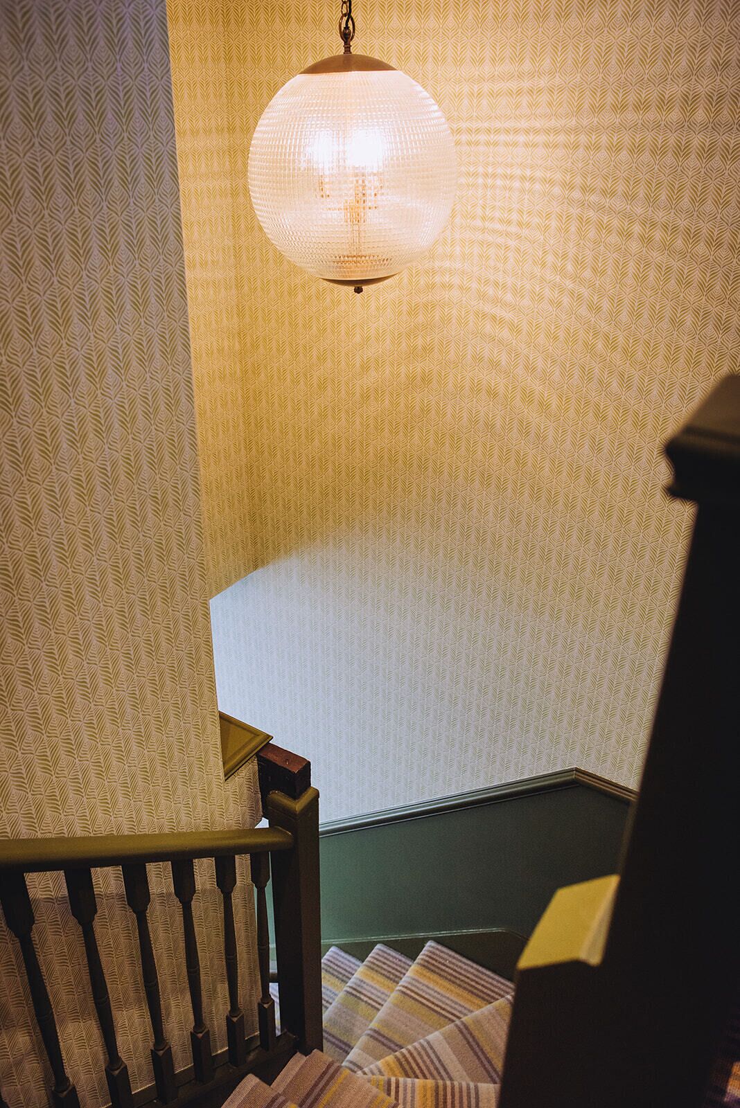 Un escalier orné d’un papier peint à motifs et surmonté d’un luminaire suspendu.