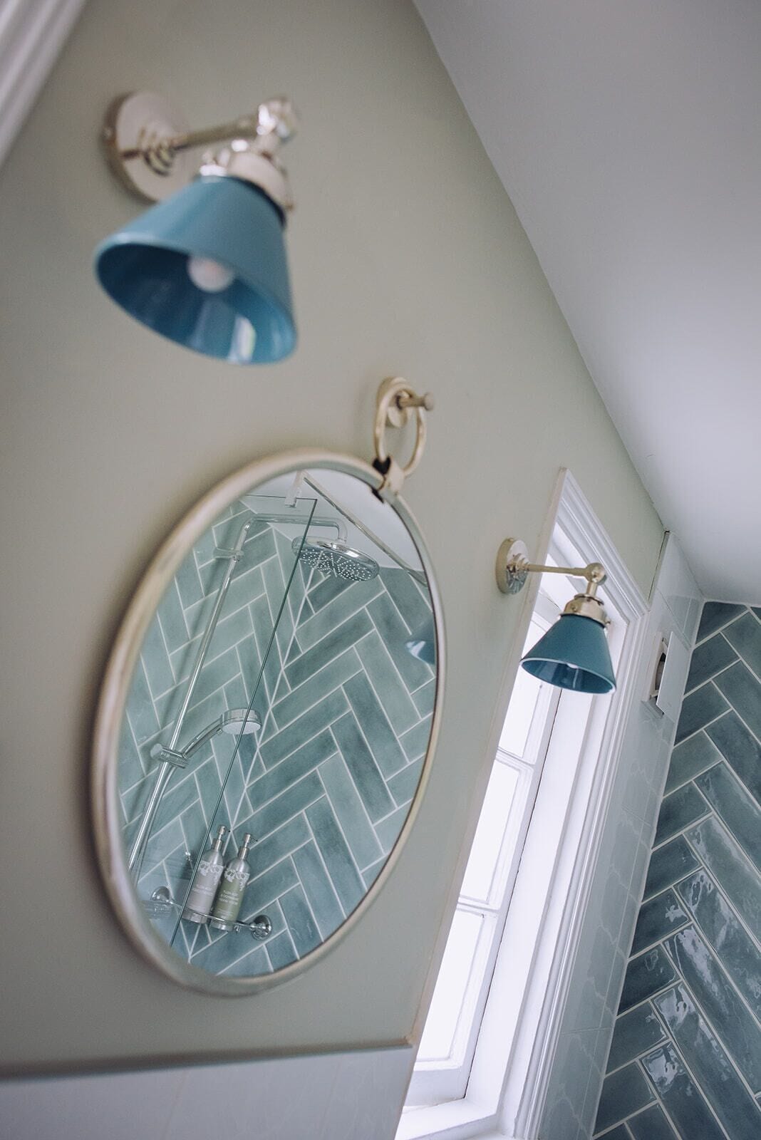 Un baño con salpicadero de azulejos tipo espiga, un espejo redondo con diseño geométrico y dos apliques de pared.