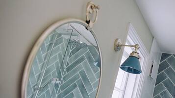 Un baño con salpicadero de azulejos tipo espiga, un espejo redondo con diseño geométrico y dos apliques de pared.