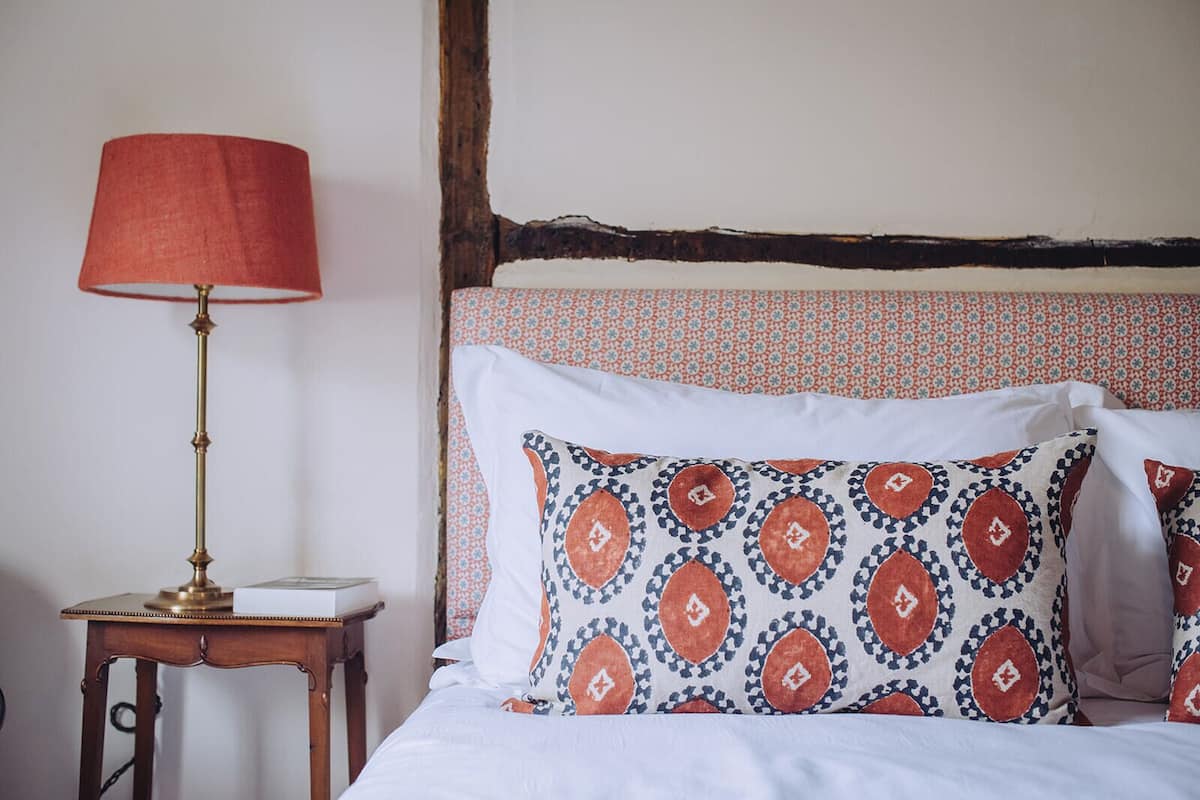 A bed with patterned pillows, a bedside table with a lamp, and a wooden headboard.
