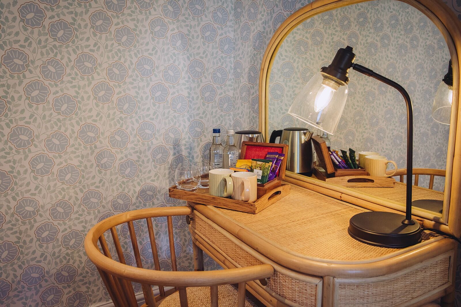 A wooden desk with a mirror, a lamp, and various items including a kettle, mugs, and a tray with snacks.