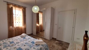 A bedroom with a bed, a mirror, a hanging light fixture, and a door leading to another room. - Villetta Lorena 100mt from the sea, Salento  (Marina di Mancaversa)