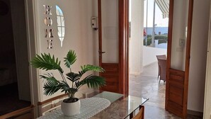 A hallway with a potted plant, a glass table, and a door leading to a balcony with a wicker chair. - Villetta Lorena 100mt from the sea, Salento  (Marina di Mancaversa)