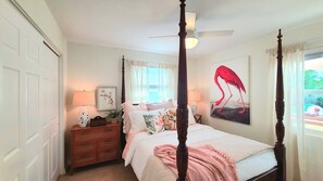 A four-poster bed with a canopy, a nightstand with a lamp, a framed picture, and a painting of a flamingo.