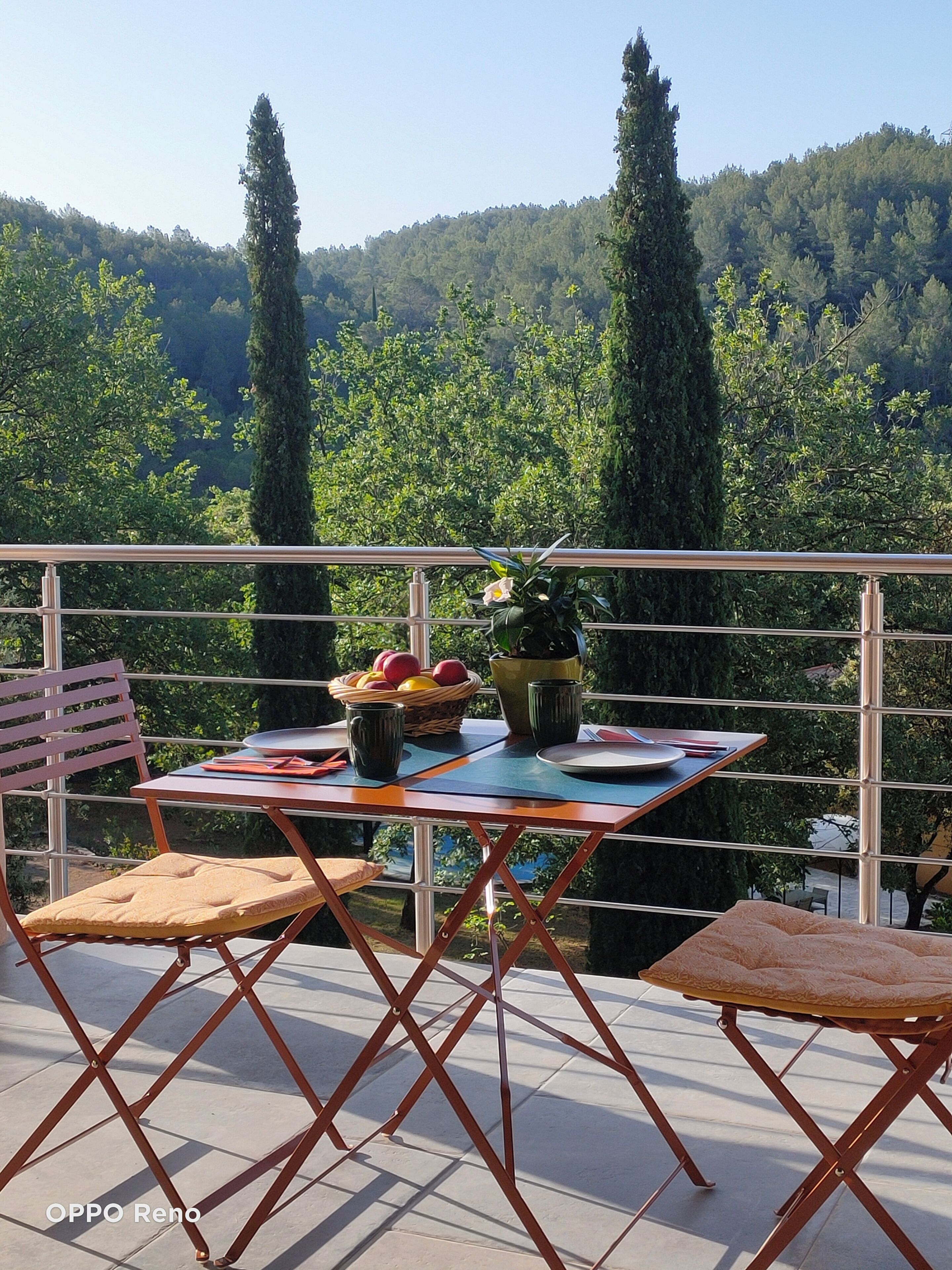 Un balcon avec une table dressée pour le dîner, entouré de chaises, donnant sur une colline boisée.