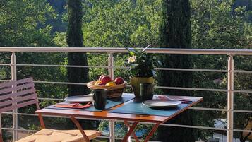 Un balcon avec une table dressée pour le dîner, entouré de chaises, donnant sur une colline boisée.