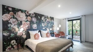 Une chambre avec un grand décor mural floral, un lit avec une literie blanche et rose, une table de chevet et une chaise près de la fenêtre.