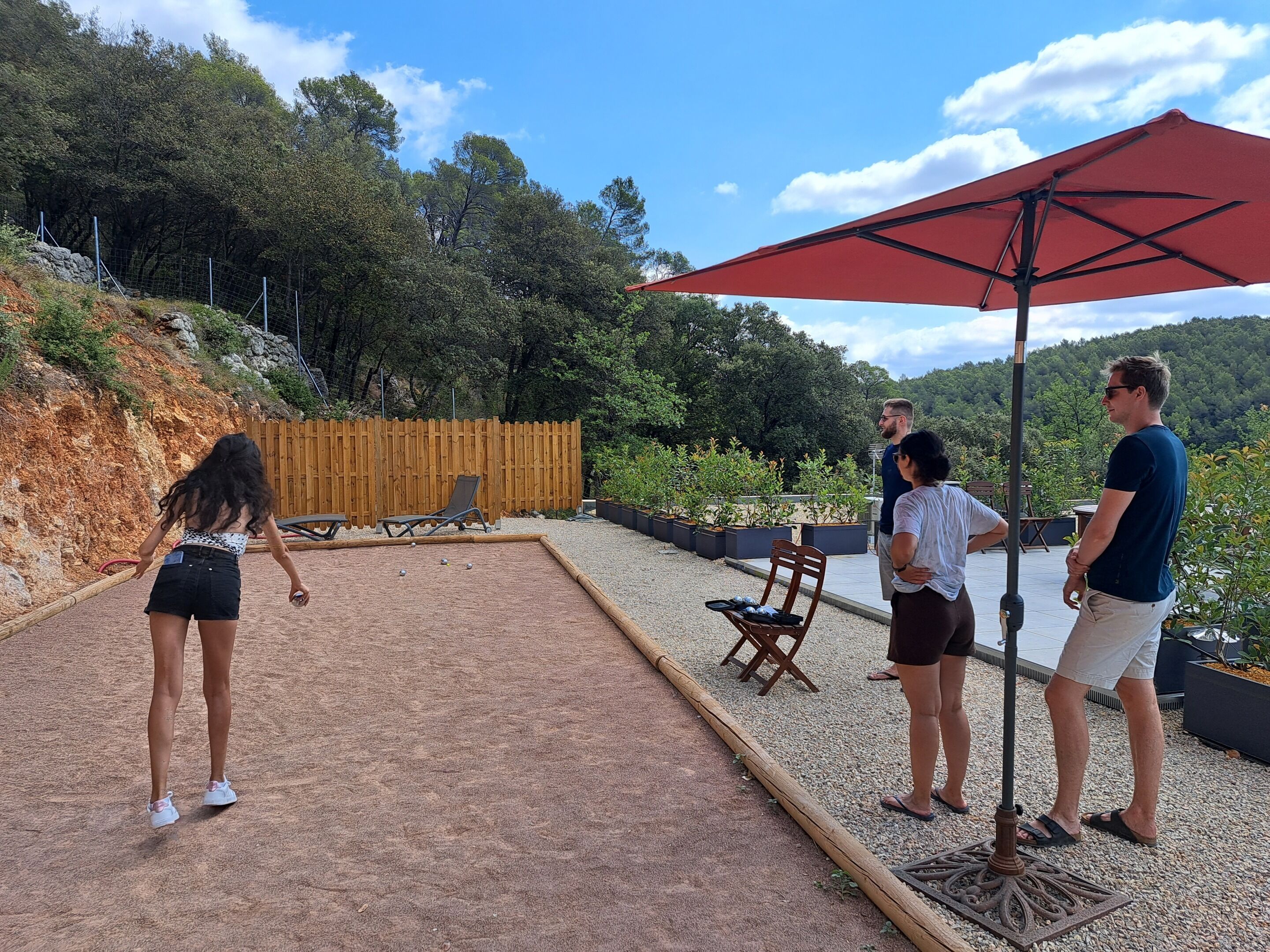 Un espacio al aire libre con una mesa de arena, sillones de descanso y una sombrilla roja.