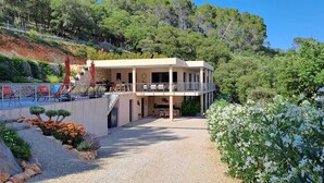 Un bâtiment à deux étages doté d’une piscine et d’un espace extérieur aménagé, entouré de verdure et de collines.