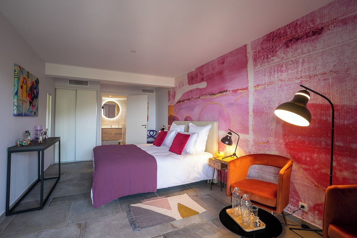 Ein modernes Schlafzimmer mit Bett, Nachttisch, Lampe und einem großen abstrakten Gemälde an der Wand.