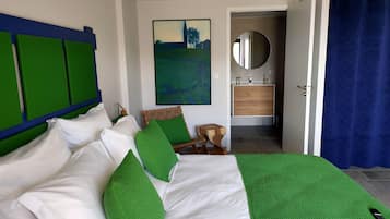 Une chambre à coucher avec un lit, des oreillers verts, une tête de lit en bois, un tableau, un miroir, une armoire en bois et un rideau bleu.