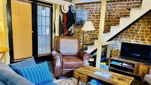 Un salon chaleureux avec un fauteuil en cuir, un canapé bleu, une table basse en bois et un téléviseur.