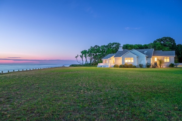 A two-story house with a porch, a satellite dish, and a view of the ocean at dusk.