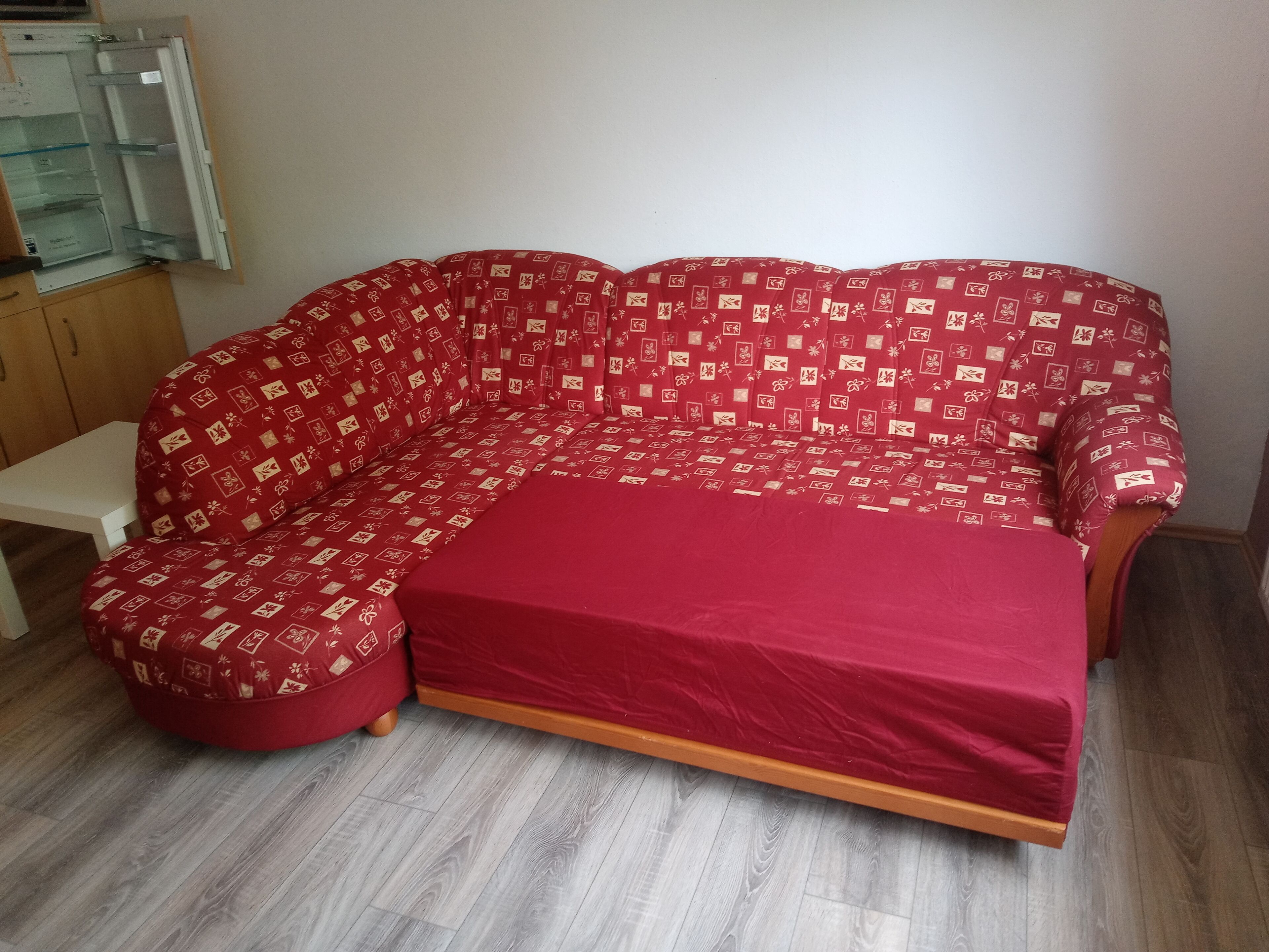 Un sofá rojo con funda estampada en una habitación con suelo de madera y pared blanca.
