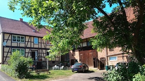 A traditional half-timbered house with a paved driveway and parked cars.