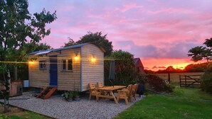 A small wooden cabin with a gravel patio, a table, and chairs. - Luxury romantic shepherd's hut - hot tub and Aga  (Camelford)