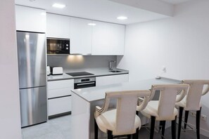 Une cuisine moderne avec des meubles blancs, des appareils en acier inoxydable et un coin bar équipé de tabourets.