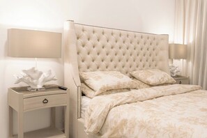 Une chambre à coucher avec une tête de lit capitonnée, une table de chevet avec une lampe et un lit recouvert d’une literie à motifs floraux.