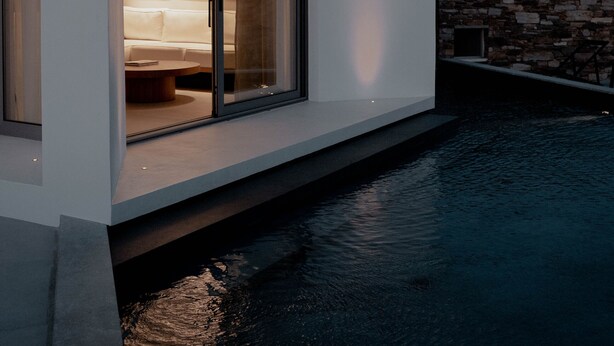 A modern house with a glass door leading to a living area with a sofa and a coffee table. - Pnoes Tinos  (Tinos)